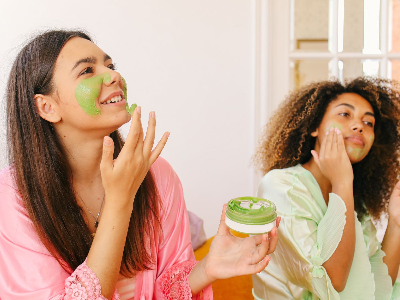 Two women putting a green face mask on their face