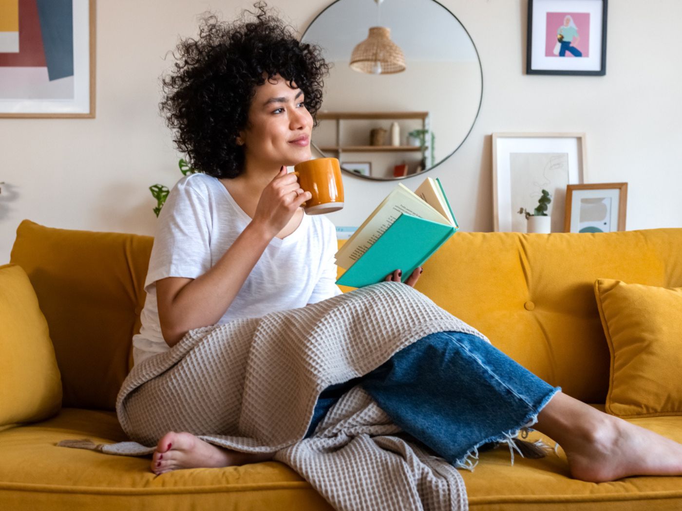 Woman on a couch with a book and mug and blanket