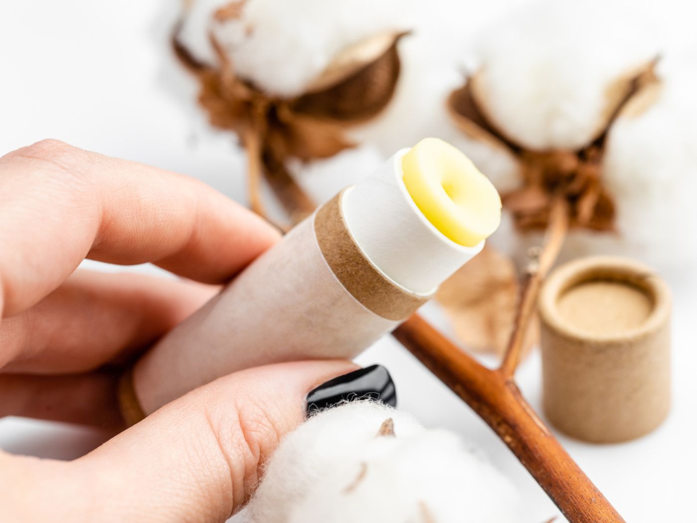 Container of chapstick with natural wrapping being held by a left hand with painted nails