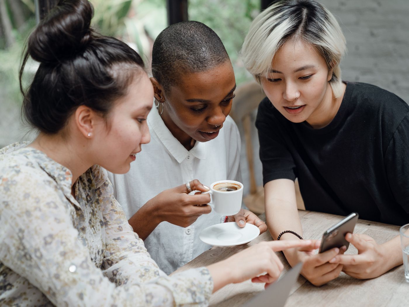 Three people looking at social media on a phone while having espresso