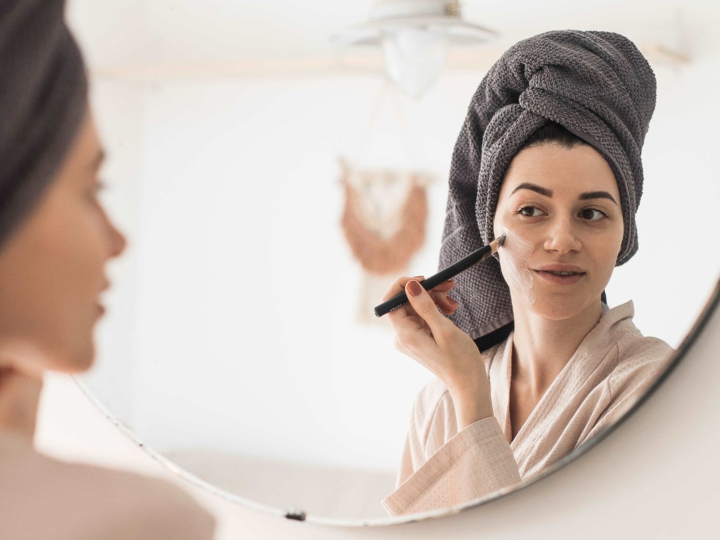 Woman with a gray towel on her head applying a face mask