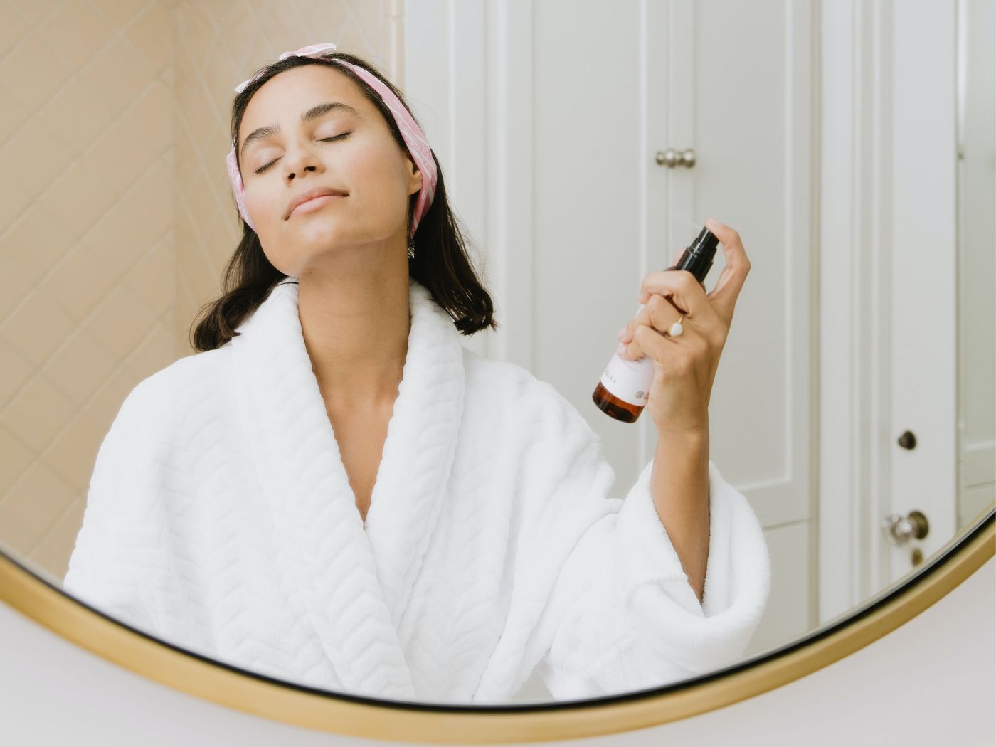 Woman using body spray in bathroom mirror