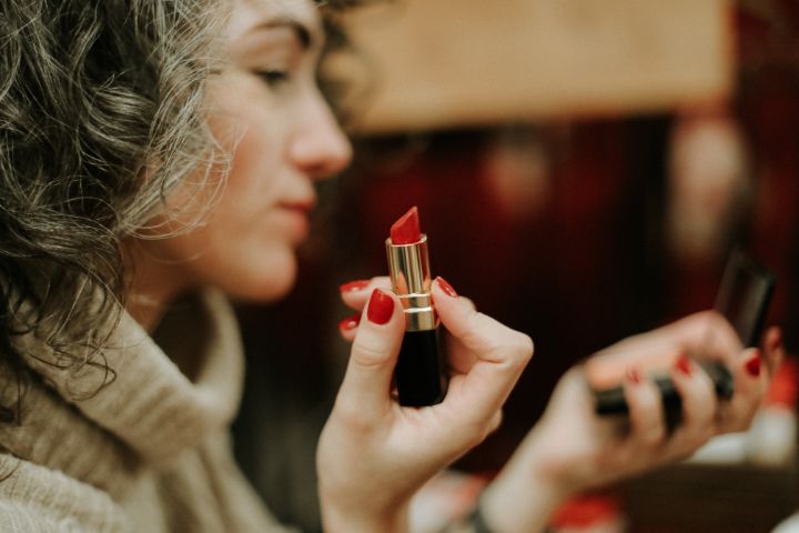 Woman holding a used lipstick while looking into a hand mirror