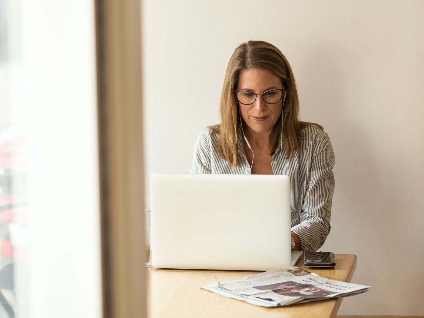 Woman working on a computer with headphones in and a newspaper in front of her