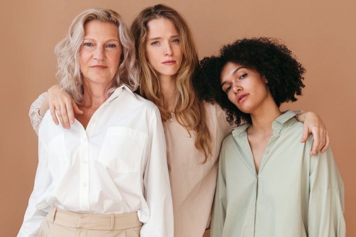 Three women of varying ages standing together in neutral outfits.