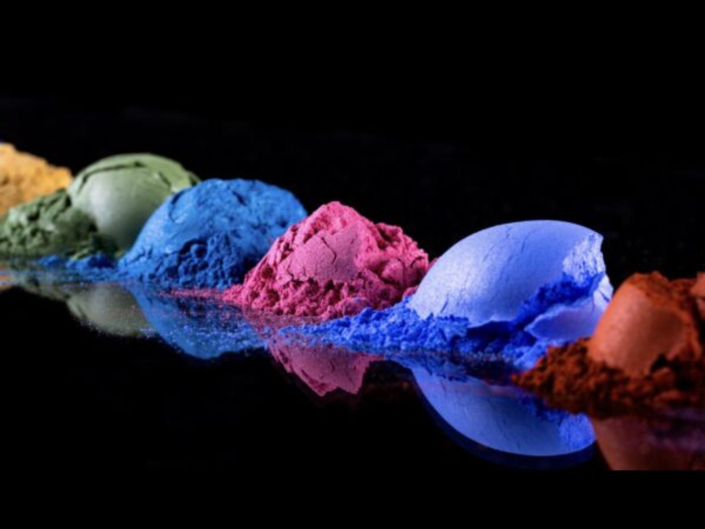 Small piles of colorful eyeshadows across a black table and background