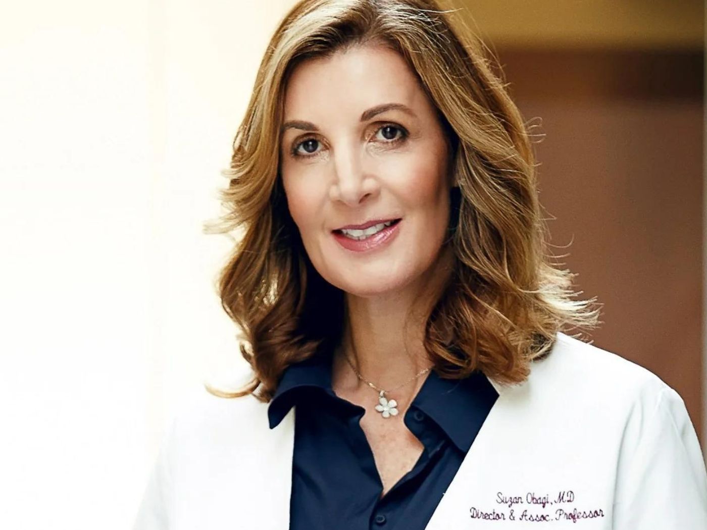 Female dermatologist, Dr Suzan Obagi, wearing a white doctor's coat embroidered with her name.