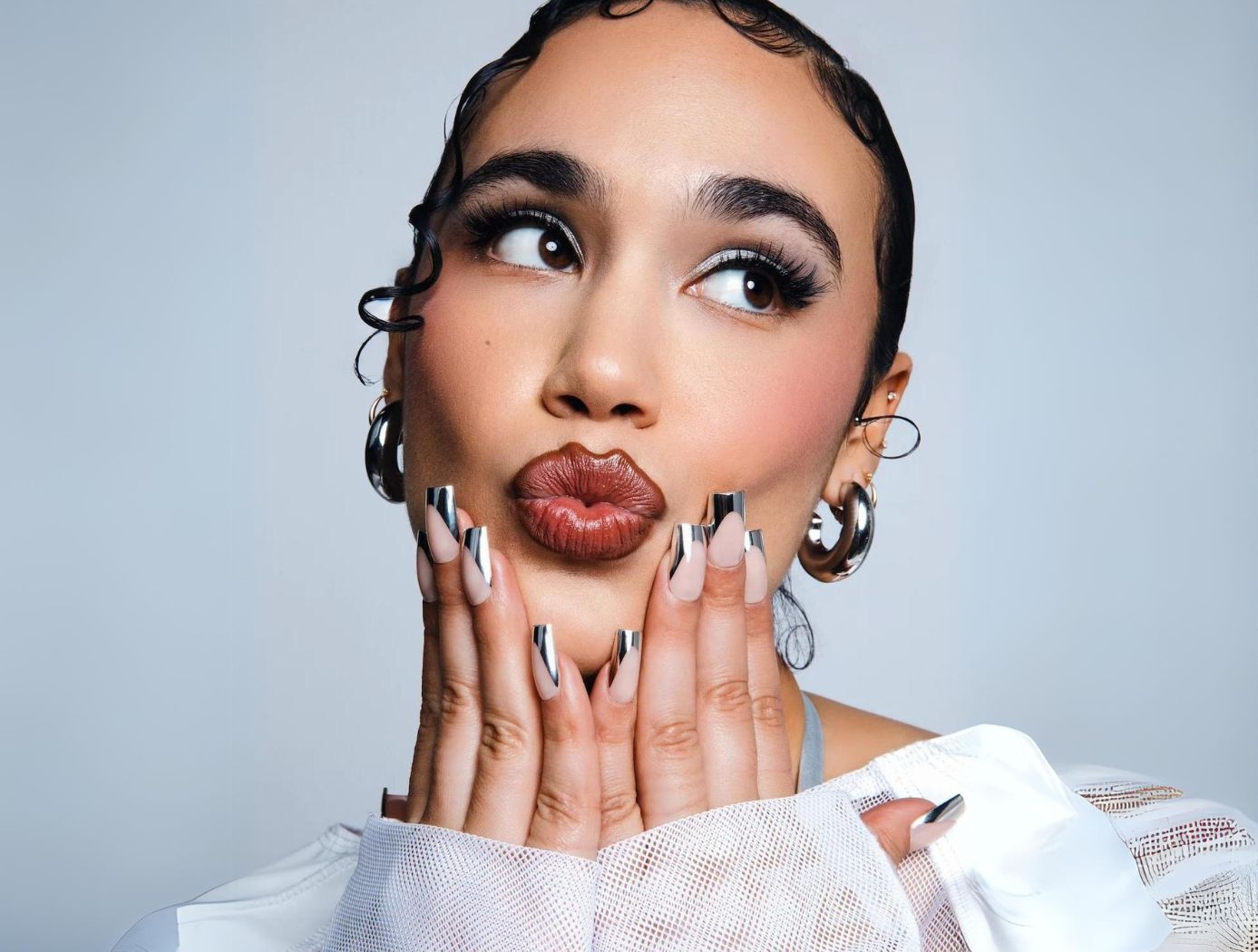 Woman with silver-tipped squoval-shaped nails manicure, wearing a white blouse.