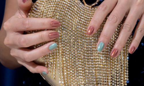 Hands holding a beaded sparkling handbag, with nails painted alternately with teal and brown metallic polish.