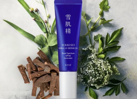 A tube of blue Sekkisei sunscreen placed on top of a selection of natural herbs and extracts.